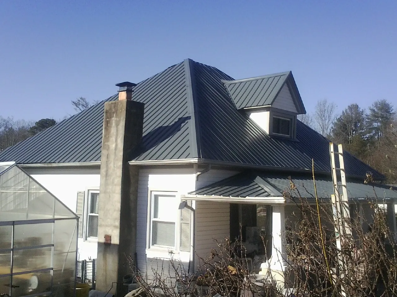 Dark blue standing seam metal roof on a white farmhouse with dormer — Slate & Tile Roof Repair by Roofing Brothers in Coeburn