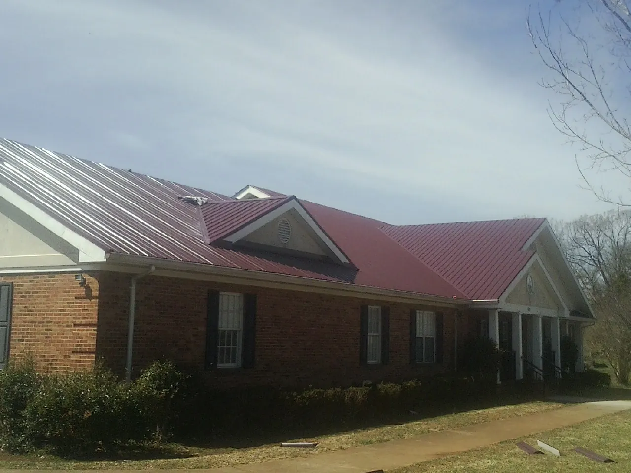 Red metal roof with gabled entries on a long brick building, from a Hail Damage Roof Repair job in Coeburn