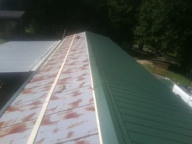 Old rusted panels beside newly installed green metal roofing — Wind Damage Roof Repair by Roofing Brothers in Coeburn
