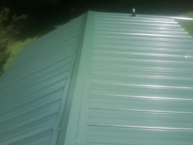 New green metal panels meeting at the ridge of a roof — Flat Roof Repair work by our crew in Coeburn