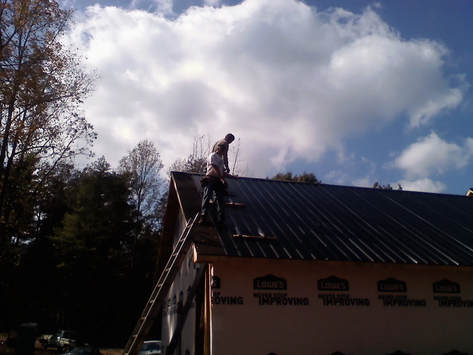 Roofer fastening dark metal panels high against a cloudy sky, from a Roof Inspection job in Coeburn