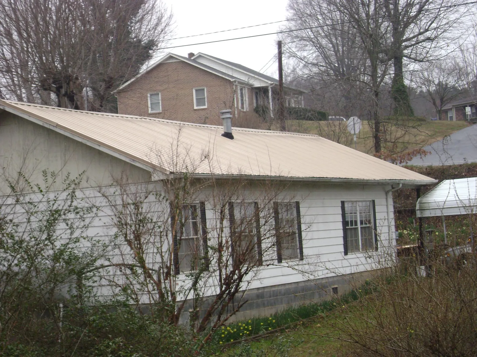 Tan metal roof on a white sided house set into a hillside — Commercial Roofing by Roofing Brothers in Coeburn