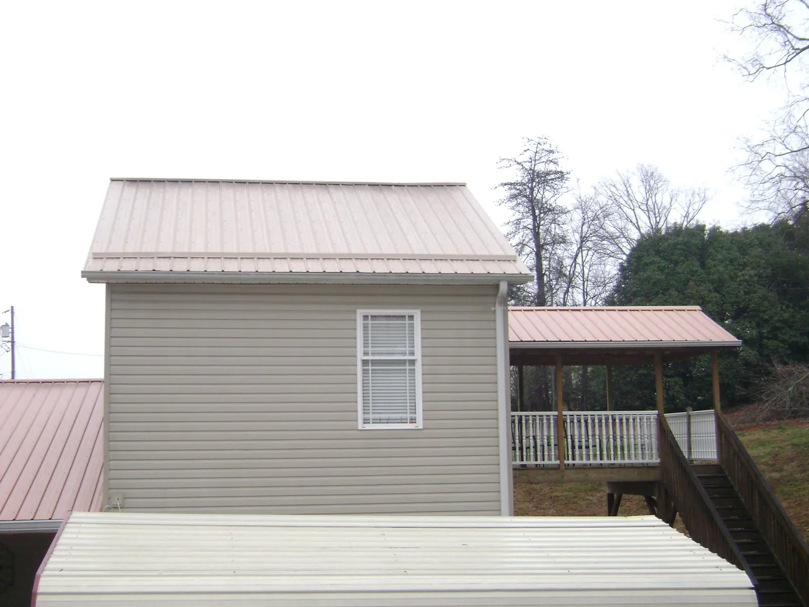 Tan metal roofs on a two story addition and attached porch, from a Roof Replacement job in Coeburn